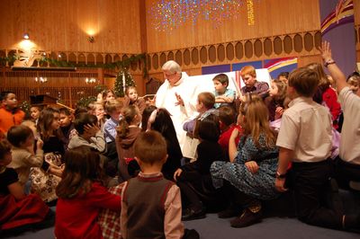 A priest surrounded by children in a church setting during a gathering.