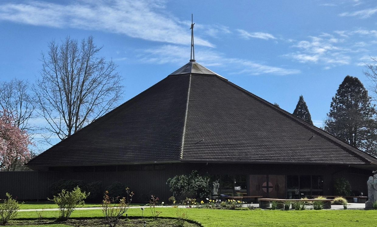 A large, pyramid-shaped church building with a cross on top under a blue sky.