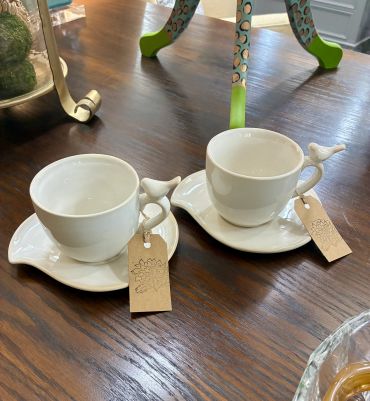 Two white ceramic cups with bird-shaped handles on matching saucers.