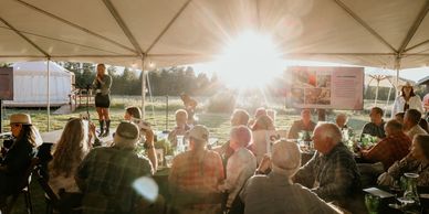 Outdoor event with a speaker under a tent during sunset.