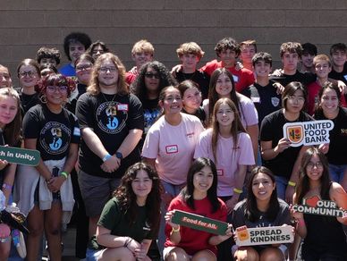 A diverse group of smiling young people holding community and kindness signs.