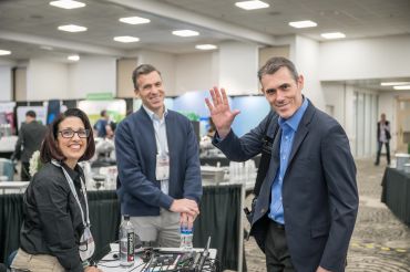 Three colleagues at a conference table, one waving.