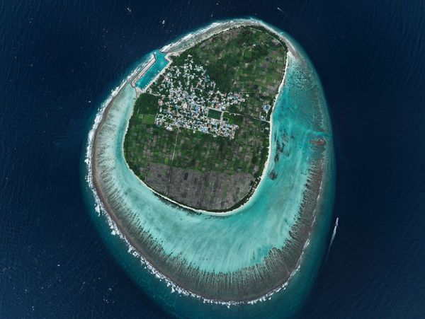 Aerial view of a small inhabited island surrounded by turquoise waters and coral reefs.