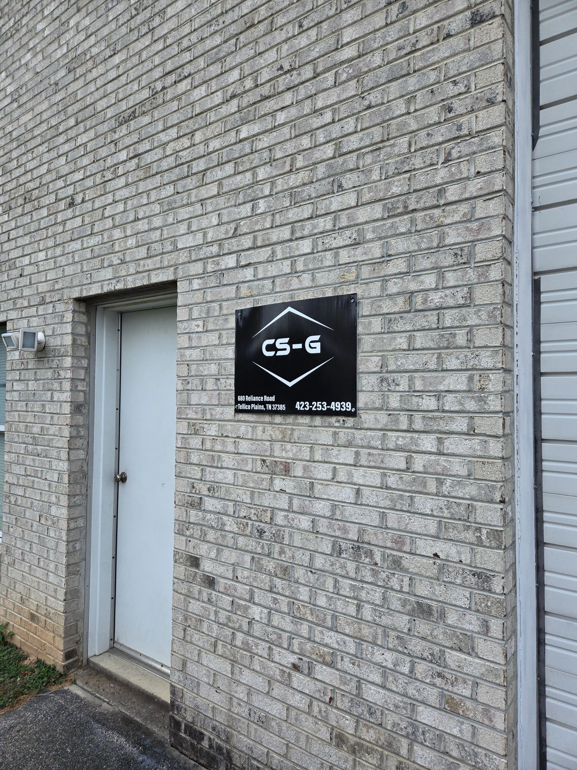 A gray brick wall featuring a black sign for "CS-G" with contact information.