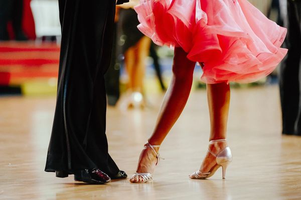 Close-up of ballroom dancers' feet, woman in pink dress and man in black trousers.