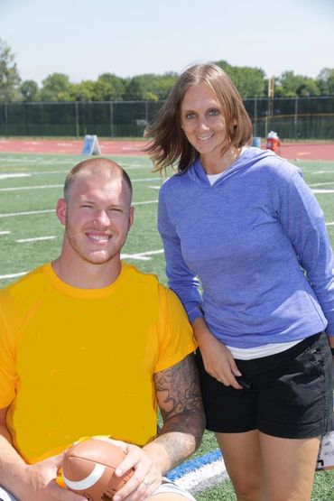 A man in a yellow shirt sitting on a football field with a woman standing beside him.
