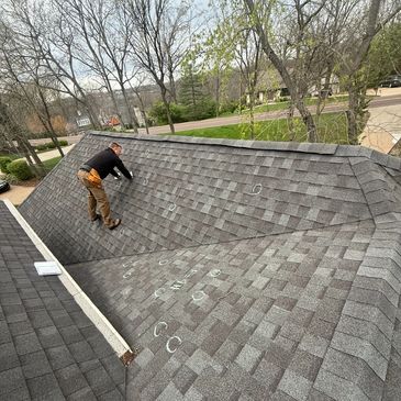 Man inspecting a roof with chalk markings on shingles.