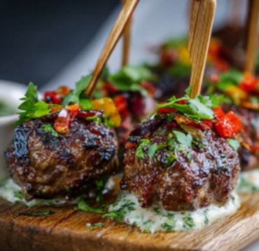 Grilled meatballs garnished with herbs and peppers on a creamy sauce.
