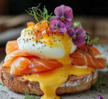 Poached egg with runny yolk over smoked salmon on toasted bread, garnished with edible flowers.