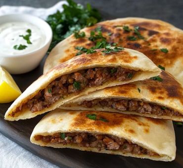 Stuffed flatbread with minced meat and herbs, served with a yogurt dip and lemon wedge.