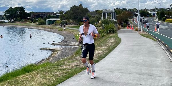 A man runs along a waterfront path under a partly cloudy blue sky.