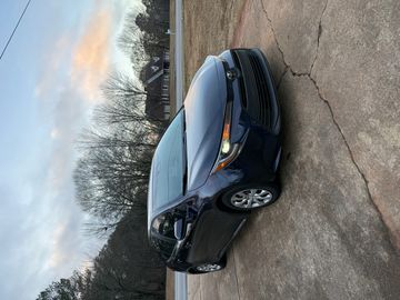 A dark blue sedan parked on a cracked driveway during sunset.