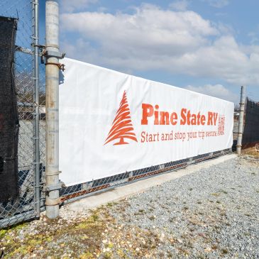 Outdoor fence banner advertising Pine State RV with a pine tree logo.