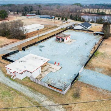 Aerial view of a fenced property with two buildings and gravel ground.