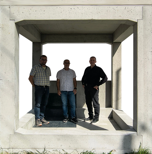 Three men posing inside a concrete structure on a sunny day.