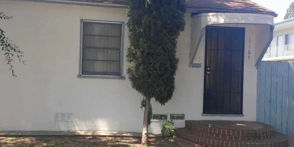 A white house with a small porch and a tree. 