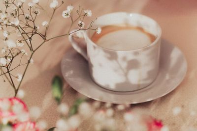 a white coffee cup and saucer with a cappuccino and flowers