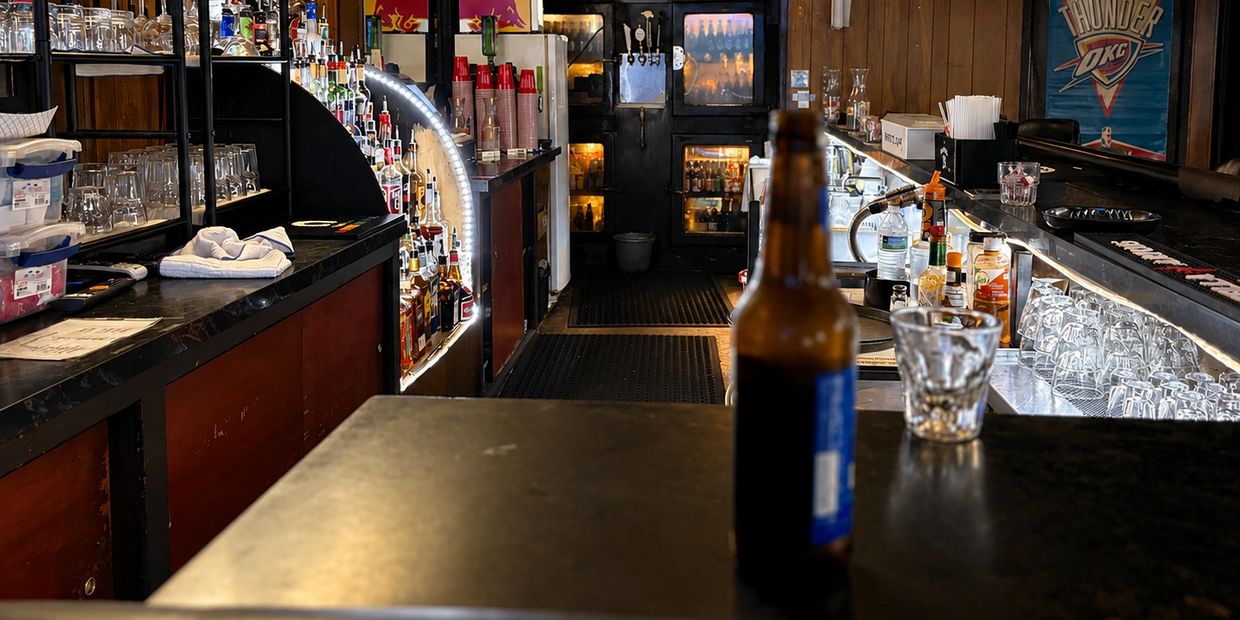 Interior of a bar with bottles, glasses, and an Oklahoma City Thunder poster.
