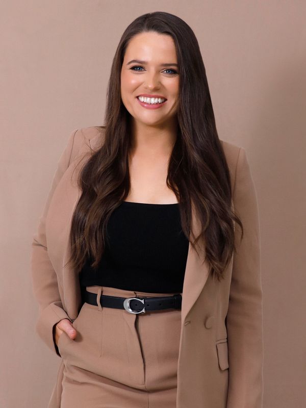 Smiling woman wearing a beige suit and black top against a beige background.