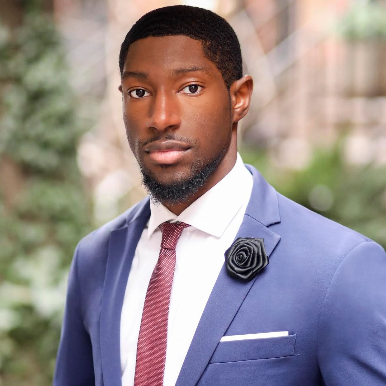 Confident man in a blue suit and red tie with a black rose pin.