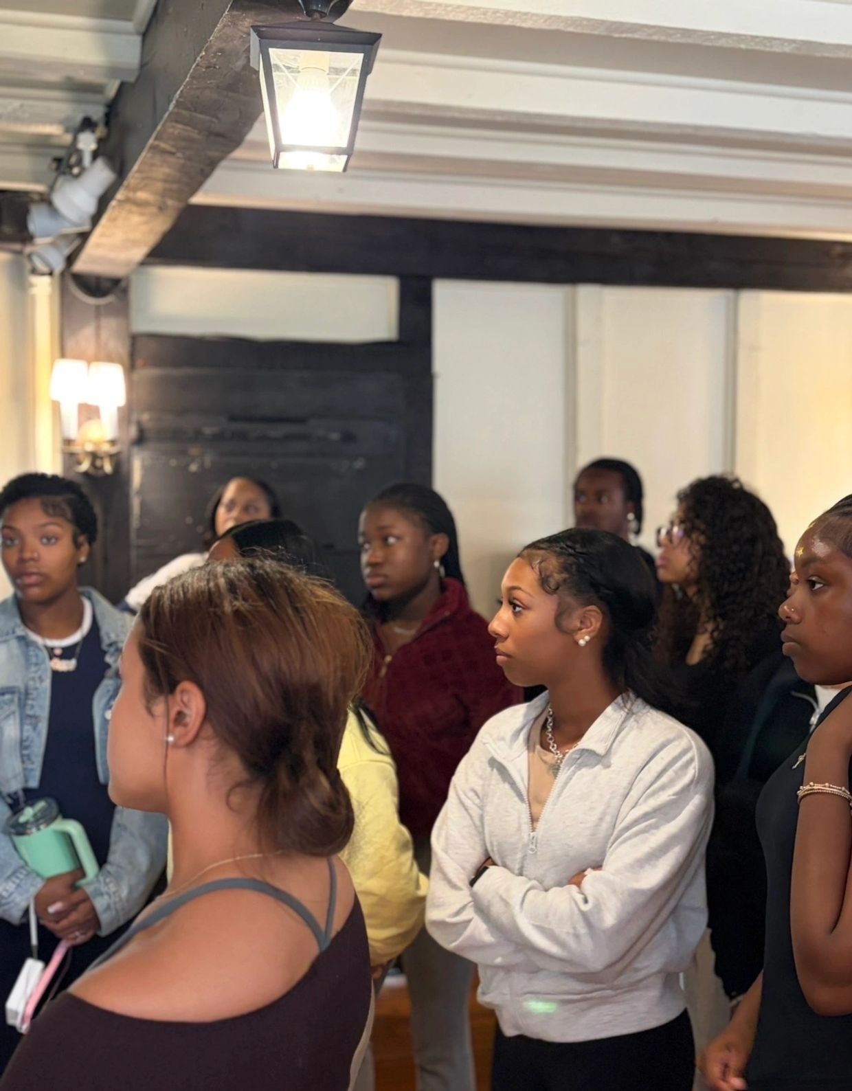 A group of young women attentively listening indoors under warm lighting.