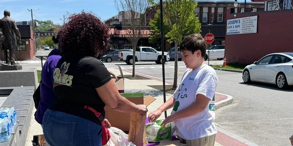 People distributing food bags outdoors on a sunny day.