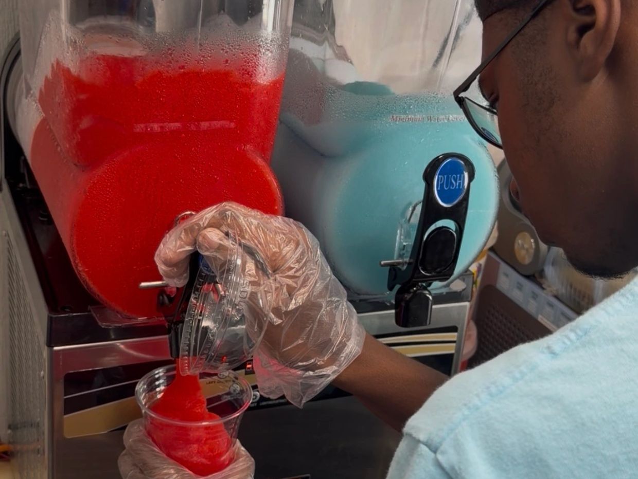 Person pouring a red slushie into a cup.