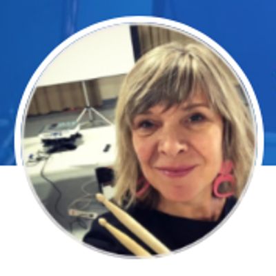 Woman holding drumsticks smiling in a music studio.