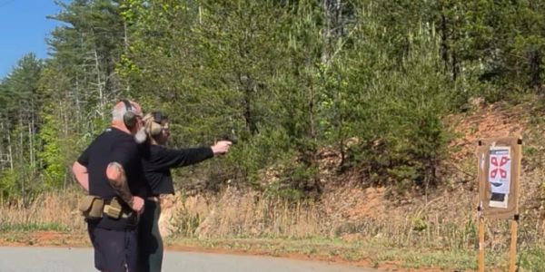 Two people at an outdoor shooting range aiming at a target.