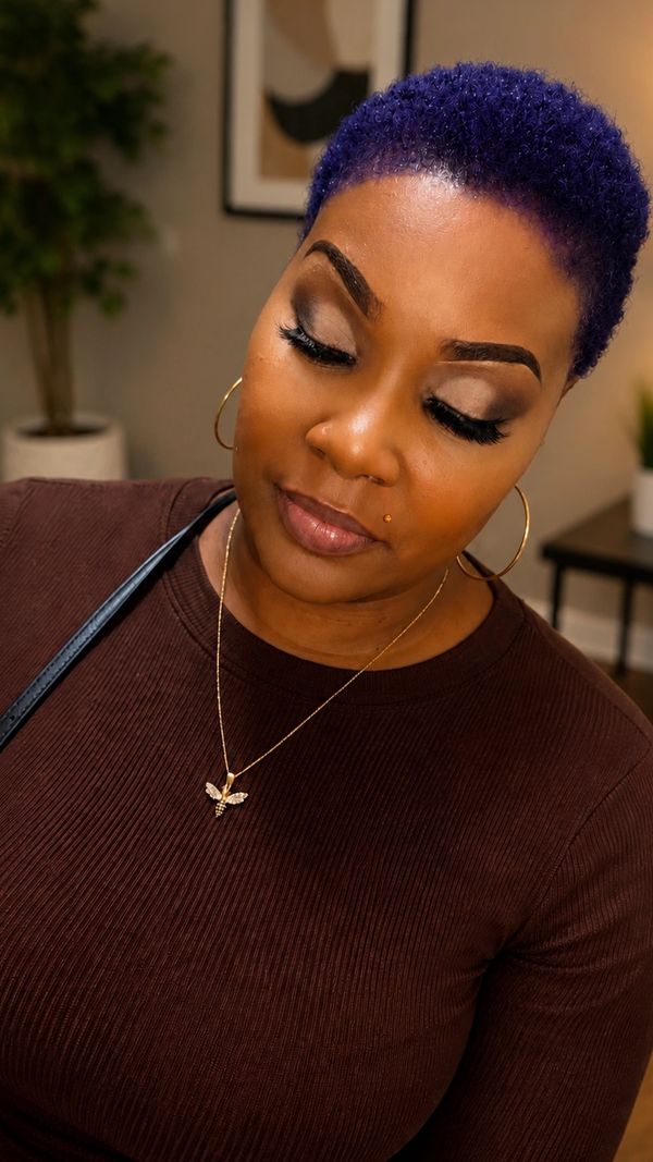 Woman with purple hair and gold bee necklace in cozy indoor setting.