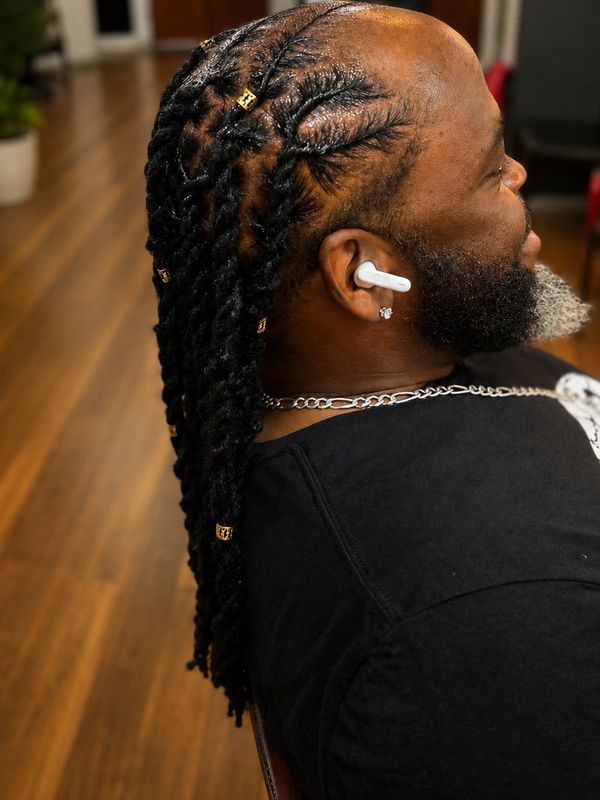 Man with detailed twisted braids adorned with gold cuffs and wearing wireless earbuds.