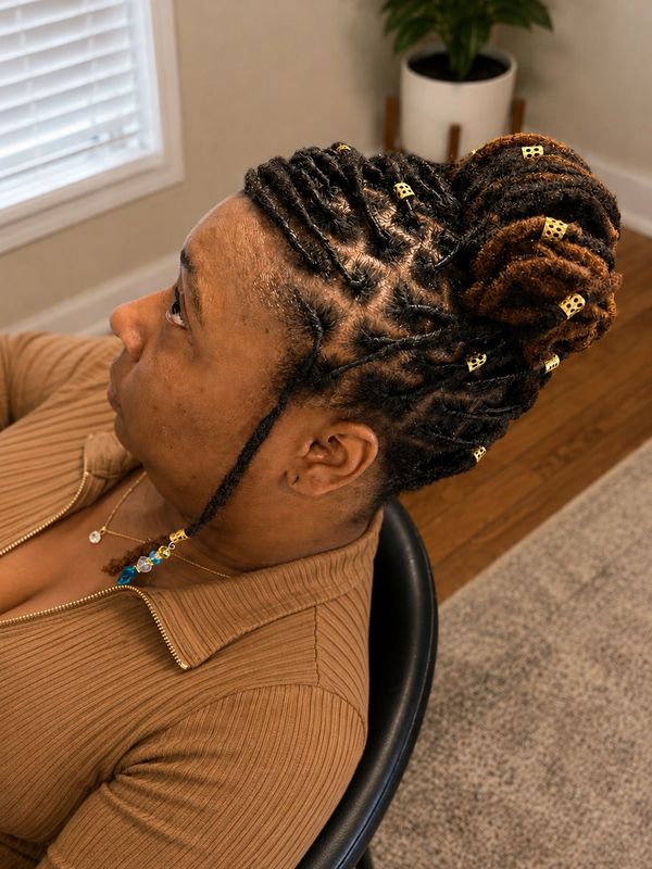 Woman with intricately braided hair styled in a bun with golden hair cuffs.