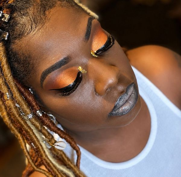 Close-up of a woman with vibrant orange eye makeup and silver lipstick.