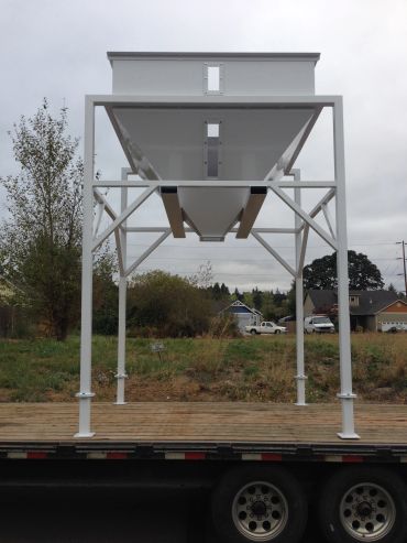 White industrial metal hopper on a flatbed trailer.