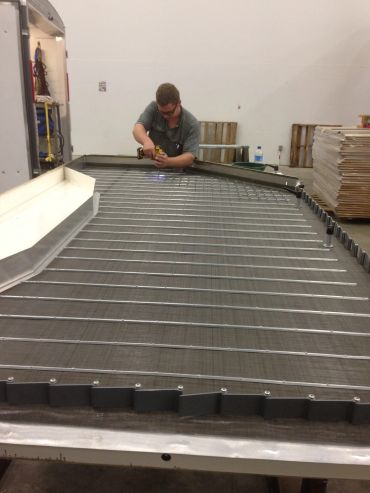 Man working on a large metal grill or frame indoors.