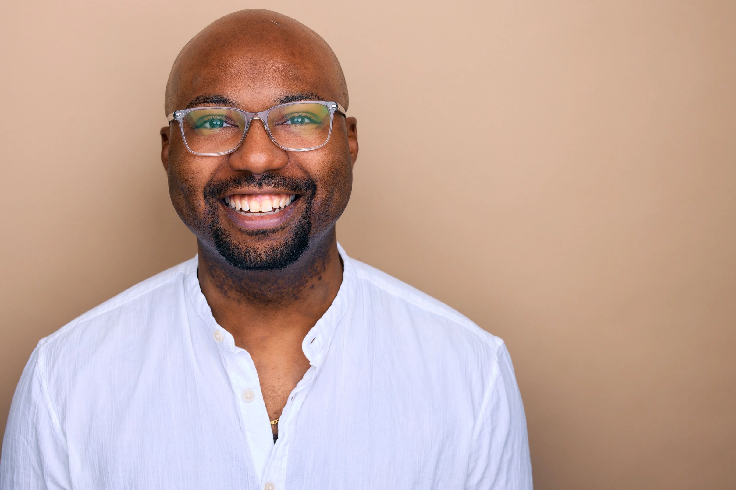 Smiling man with glasses in white shirt against beige background.