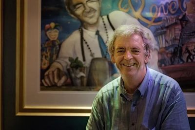 a photograph of chris mcmillian sitting in front of jill degroff's watercolor portrait chris mcmilli