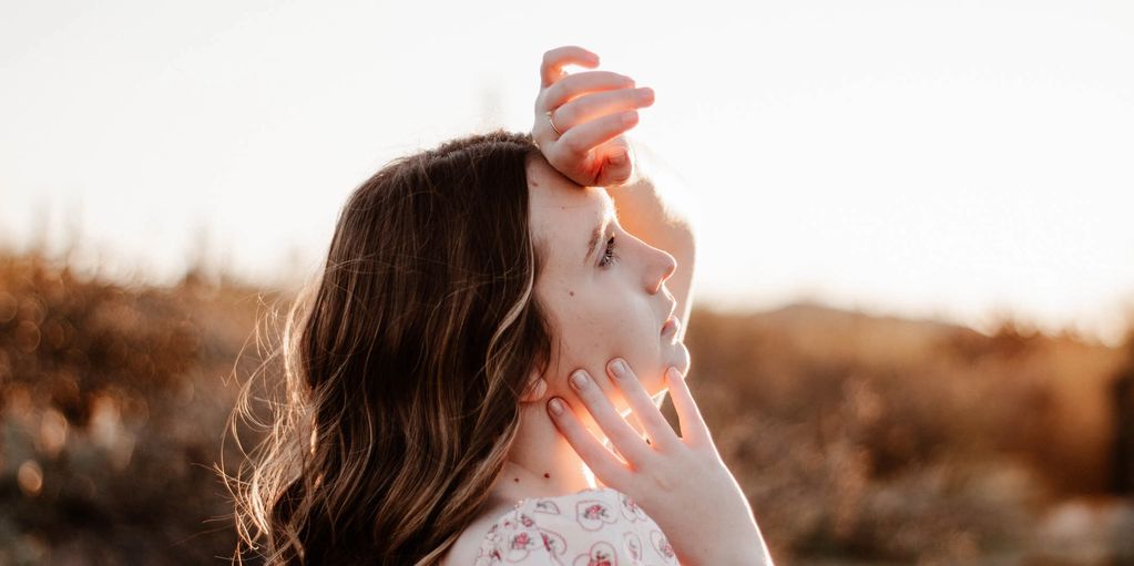 Woman gazing into the distance with hand on forehead at sunset.