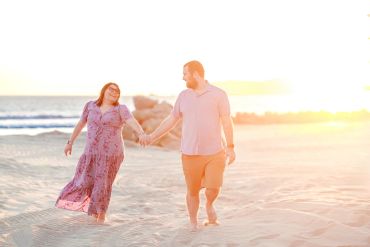 Couple holding hands and walking on the beach at sunset.