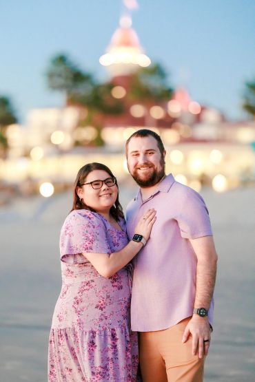 Couple smiling together near a brightly lit building.