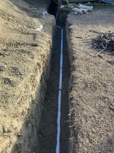 A trench with a white PVC pipe laid underground.