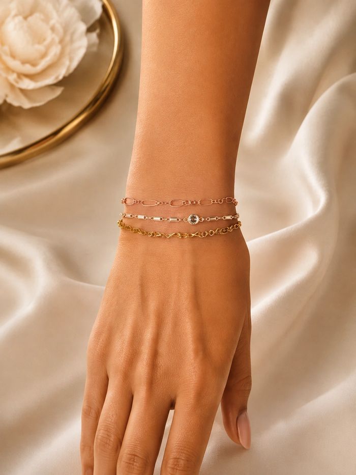Close up of a wrist wearing three delicate permanent bracelets in rose gold, silver, and gold tones.