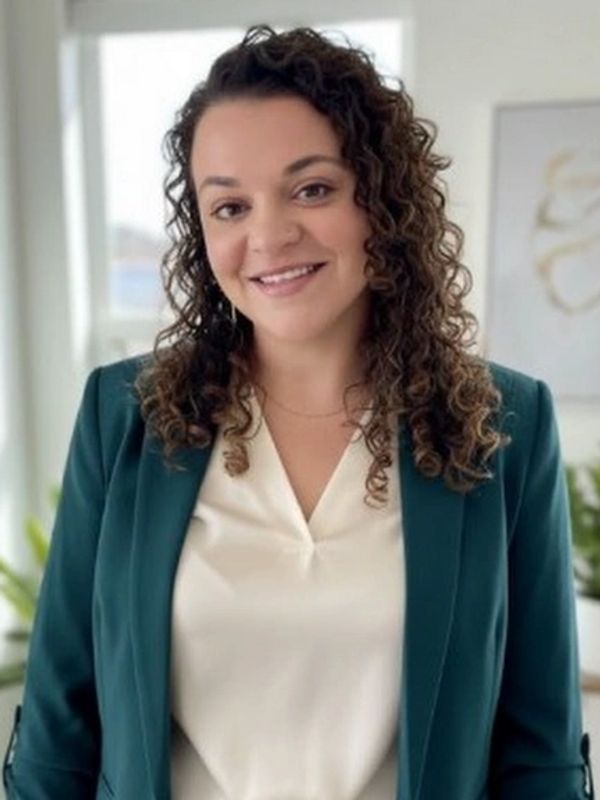 Smiling woman with curly hair in a green blazer and white blouse.