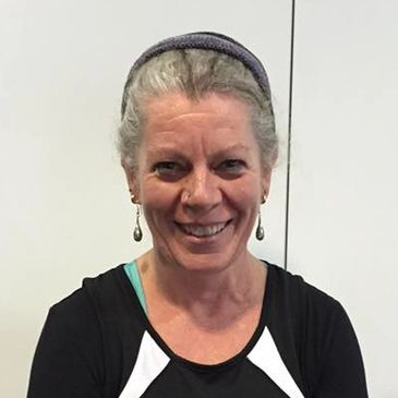 Smiling woman with gray hair wearing earrings and a headband.