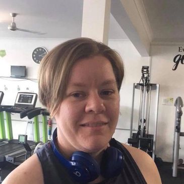 A woman wearing headphones at the gym, smiling slightly.
