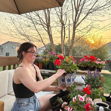 A woman gardening with colorful flowers at sunset on a patio.