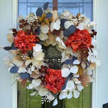 A vibrant floral wreath with orange and cream flowers on a glass door.