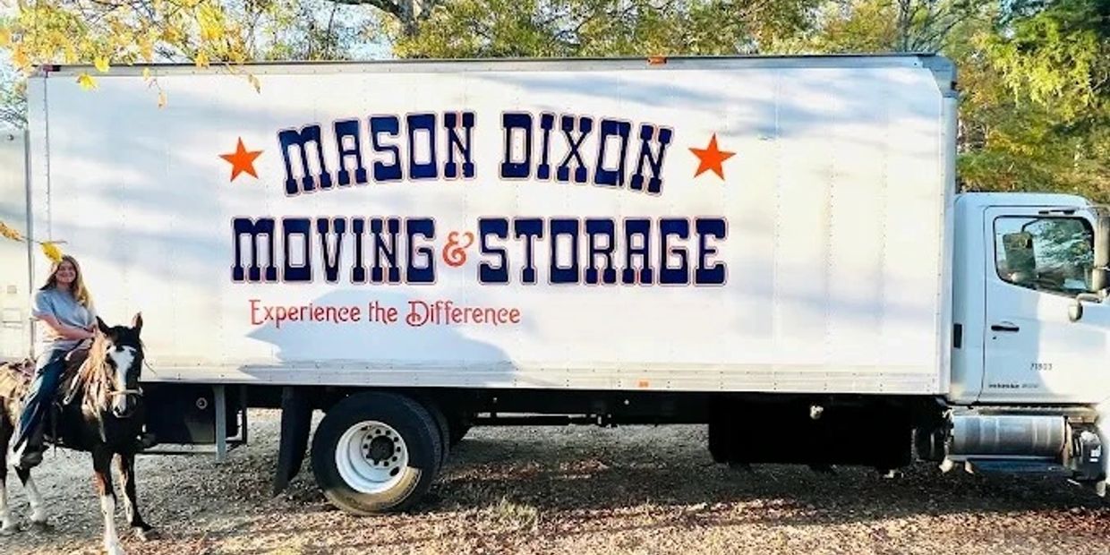A woman rides a horse beside a Mason Dixon Moving &amp; Storage truck outdoors.