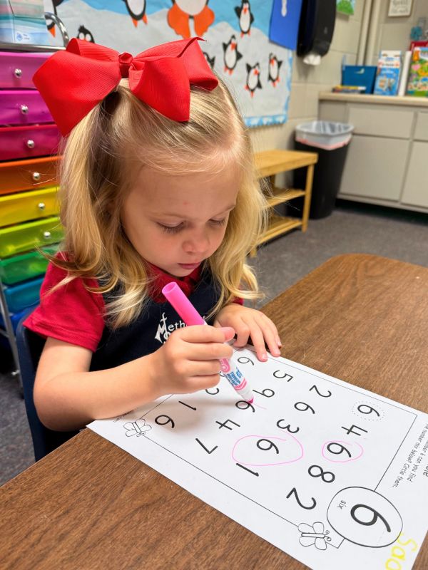 Young girl circling numbers on a worksheet with a marker.