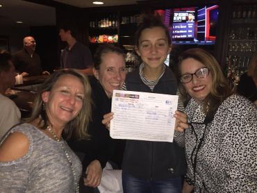 Four women smiling in a bar, one holding a paper.